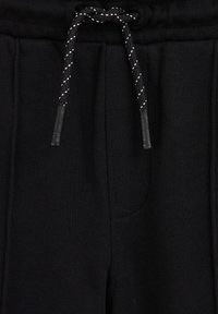 Melni sporta bikses ar teksturētu audumu, elastīgu jostu un auklu. Iekļauj sānu kabatas un brīvu piegriezumu.