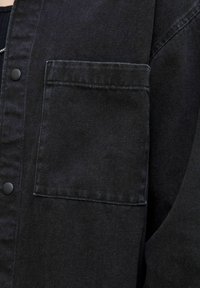 Black denim jacket featuring a button closure, structured collar, chest pocket, and subtle texture across the fabric.