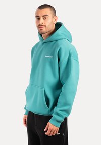 Felpa turchese realizzata in cotone misto, con tasca anteriore, cappuccio con lacci e ricamo del logo sul petto.