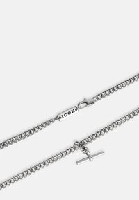 Ezüst lánc nyaklánc, összekapcsolt karikákkal, logóval ellátott címkével és kapoccsal. Simább felület, fényes kivitel.