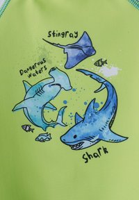 Tissu vert vif avec un graphique d'un requin, d'une raie et d'un poisson avec des effets aquarelle et un texte indiquant "Eaux dangereuses" et "requin."