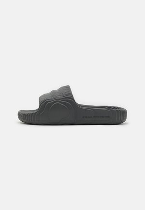Gray slide sandal with a wave-like textured upper, flat sole, and ridged pattern. Features branding along the side. Lightweight material.