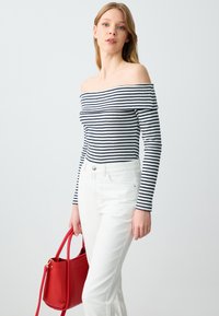Schulterfreies gestreiftes Top in Marineblau und Weiß, mit geripptem Textur, kombiniert mit weißen Jeans und einer roten Handtasche für den Kontrast.