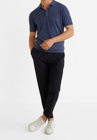 Polo à manches courtes bleu marine avec un design texturé, accompagné d'un pantalon noir fuselé et de baskets blanches. Tenue simple et moderne.