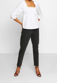 Vit blus med fyrkantig halsringning och texturerad smockning i midjan, kombinerad med svarta raka jeans och svarta sandaletter med klack och remmar.