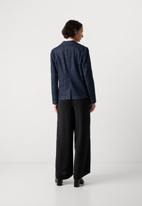 Mørk denimblazer med skreddersydd design, klipp med slag og bakventil, kombinert med vide svarte bukser. Teksturet stoff, strukturert form.