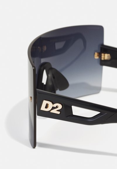 Óculos de sol oversized pretos com lentes cinzentas em degradê. Apresenta o logo "D2" em dourado e um design geométrico elegante com cortes na armação.