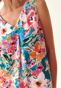 La blusa de estampado floral presenta un escote en forma de V, colores vibrantes que incluyen rosa, azul, naranja y verde, y una tela suelta y texturizada.