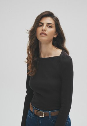 Black ribbed long-sleeve top with a square neckline, paired with high-waisted blue denim jeans and a brown belt with a metal buckle.