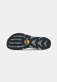 Semelle de chaussure de trail avec un grip en caoutchouc noir, présentant des crampons angulaires et un logo jaune proéminent dans la zone de la semelle intermédiaire.