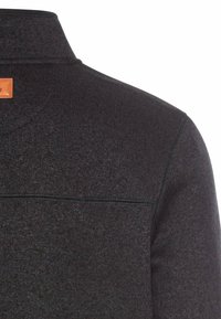 Donkergrijze gebreide trui met een hoge kraag, gestructureerde stof en een bruine leren label op de achterkant nabij de halslijn.