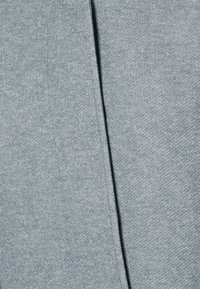 Světlě šedá látka s jemnou strukturou, s decentním melírovým vzorem a svislým švem na boku, který naznačuje tvar oděvu.