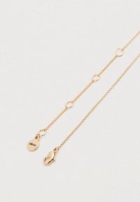 Χρυσό κολιέ πολλαπλών στρωμάτων με κυκλικό ταμπελάκι που φέρει την εγχάραξη "DKNY" και κούμπωμα αστακού. Λεπτές αλυσίδες με κυκλικά κρίκους προσθέτουν υφή.