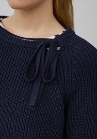 Marine gebreide trui met ribbeltextuur, ronde hals en een decoratieve strik op de schouder. Heeft een gestreepte binnenkraag.
