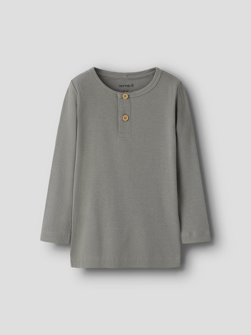 Camiseta de niño pequeña gris de manga larga con cuello redondo y dos botones marrones en la tapeta frontal, extendida sobre una superficie gris.