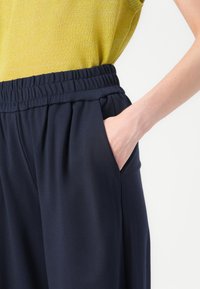 Navy blue elastic waist pants with side pockets, featuring soft fabric and pleats, paired with a textured yellow top.