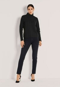 Schwarzer Rollkragenpullover aus Kabelstrick mit langen Ärmeln, kombiniert mit dunklen Jeans und schwarzen Stilettos. Glatte Textur, figurbetonter Schnitt.