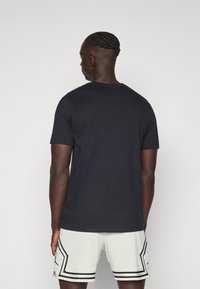 Camiseta de algodón negra con mangas cortas y cuello redondo, acompañada de pantalones cortos de malla blanca con acentos negros y una textura perforada.