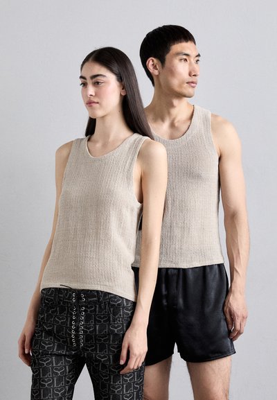 Beige ermeløse strikketopper med en teksturert finish, med rund hals. En modell kombinerer dem med svarte mønstrede bukser; den andre med svarte shorts.