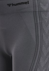 Szare legginsy sportowe z teksturowanej tkaniny, z prążkowanym pasem w talii i geometrycznymi perforowanymi wzorami po bokach.