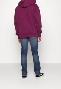 Sweat à capuche violet à coupe décontractée, porté avec un jean bleu et des baskets noires, avec des poignets et un ourlet côtelés.