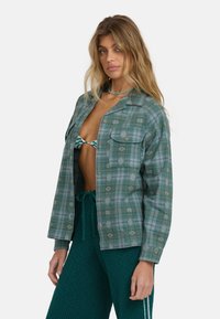 Groene geruite overhemd met een ontspannen pasvorm, met twee borstzakken en subtiele witte patronen; gedragen over een gemusterde bikini-top.