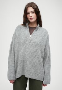 Γκρι πλεκτό πουλόβερ με ψηλό γιακά και μπροστινό μισό φερμουάρ. Διαθέτει χαλαρή εφαρμογή και μακριές μανίκια, υφή με διακριτό μοτίβο.