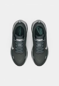 Grå idrettssko med en strukturert overflate, med snøring, myk demping og et sølvfarget swoosh-aksent. Gummiyttersåle for godt grep.