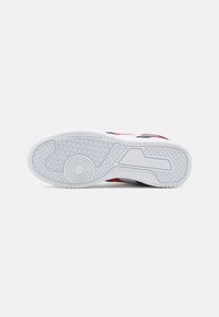 Suola di sneaker, prevalentemente in gomma bianca con grip testurizzato. Presenta un design blu e rosso, bordi lisci e motivi circolari sul fondo.