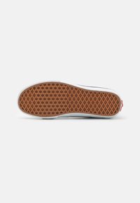 Podeszwa sneakersów Vans o fakturze plastra miodu, w jasnobrązowym kolorze, obramowana białą gumą. Czerwone akcenty logo na pięcie.