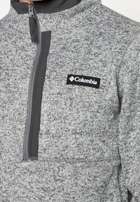 Pullover in pile grigio con zip frontale a metà, motivo testurizzato e un'etichetta nera Columbia sul petto. Accentuato con tessuto grigio scuro.