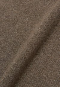 Tessuto marrone con una superficie morbida e texturizzata, che mostra sottili variazioni di tonalità. Si piega delicatamente, evidenziando il suo design spesso e lavorato a maglia.