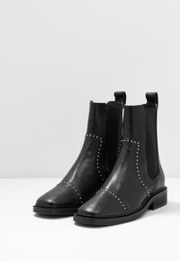 Botas de tobillo de cuero negro con un acabado texturizado, paneles laterales elásticos, detalles con tachuelas a lo largo de las costuras y un tacón bajo y apilado.