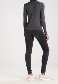 Grauer Langarmpullover mit tailliertem Design, kombiniert mit schwarzen Slim-Fit-Jeans und hellbeigen Sneakers. einfacher und minimalistischer Stil.