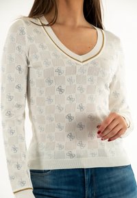 Pulover alb din tricot cu decolteu în V, având un model texturat cu pătrate albastre și desene florale, accentuat de o margine aurie la guler.