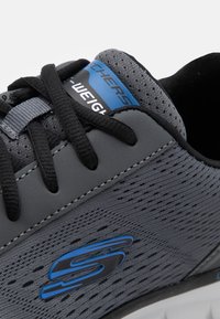 Gray athletic shoe made of breathable mesh and synthetic material, featuring black laces and a blue logo accent on the side.