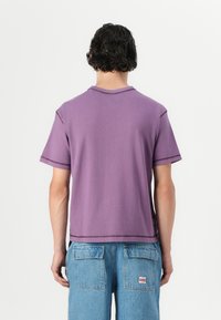 Purple cotton t-shirt with short sleeves, a round neckline, and contrasting stitching. Worn with blue denim shorts featuring patch pockets.