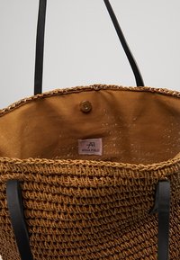 Woven torba na ramię w kolorze jasnobrązowym z teksturowaną powierzchnią, czarnymi skórzanymi uchwytami oraz podszewką z tkaniny z wewnętrzną metką z logo.