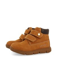 Bottes en daim marron avec deux sangles Velcro, bout arrondi, col rembourré et semelle en caoutchouc texturée. Comprend des coutures décoratives et un détail de logo.