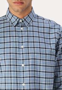 Blue and black checkered button-up shirt featuring a classic collar and white buttons, made from lightweight fabric with a smooth texture.