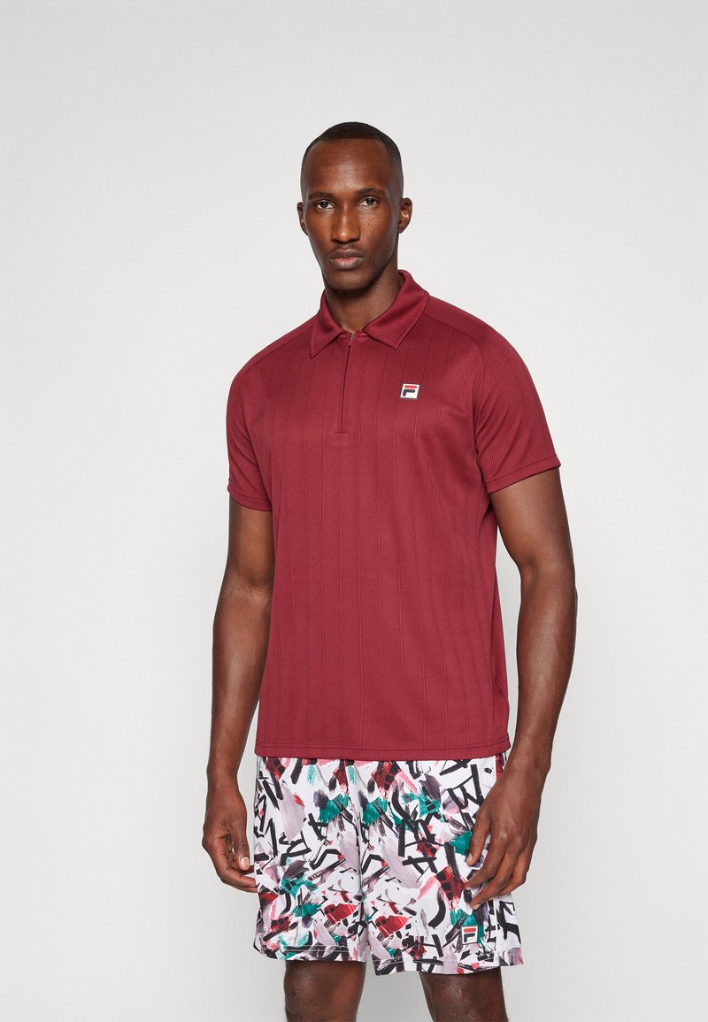 Bordo polo majica kratkih rukava s teksturiranim prugama, s ovratnikom i malim logotipom. Uparena s uzorkovanim šorcima u bijeloj, zelenoj i crvenoj boji.