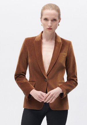 Blazer en velours marron avec des revers à cran, fermeture à un bouton, deux poches avant et coupe ajustée, associé à un pantalon noir.