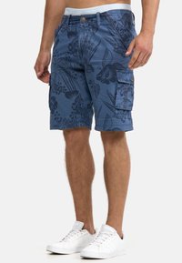 Blue cargo shorts in lightweight fabric with a floral pattern, featuring multiple pockets and a drawstring waistband. Worn with white sneakers.