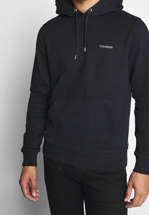 Haut à capuche noir en coton avec une poche frontale, des poignets côtelés et un capuchon à cordon ; présente un petit logo blanc sur la poitrine.