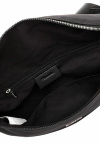 Vnitřek černé kabelky ukazující kapsu na zip se stříbrným jezdcem na zipu a látkovou štítkem uvnitř kapsy.