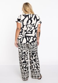 Lockere schwarze und weiße gemusterte Kombination mit abstrakten Designs. Das Oberteil hat kurze Ärmel; die Hose ist weit geschnitten und mit grafischen Details versehen.