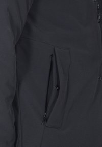 Giacca nera imbottita con finitura opaca. Presenta una tasca con zip e chiusura a bottoni a pressione, evidenziando elementi di design pratico.