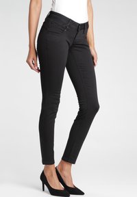 Vaqueros ajustados negros hechos de mezclilla con una textura suave. Presentan una cintura de talle medio y dobladillos remangados, combinados con tacones altos negros.