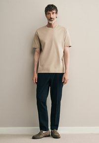 Beige, rövid ujjú póló sötétkék nadrággal és barna velúr mokaszinokkal párosítva. Puha anyag, laza fazon, minimalista dizájn.