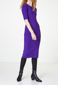 Robe midi en tricot violet à manches courtes, coupe ajustée, et col rond, accompagnée de bottines noires et de collants opaques noirs.